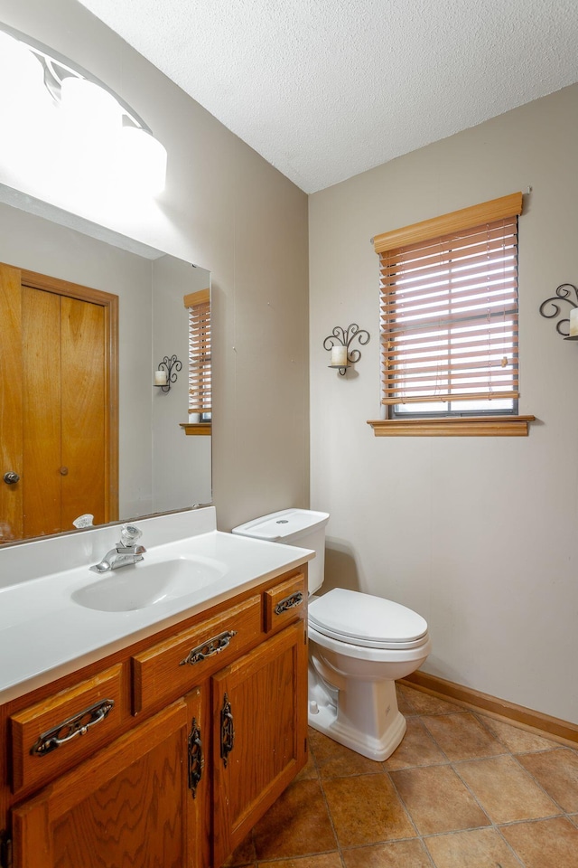 bathroom with a textured ceiling, vanity, toilet, and baseboards