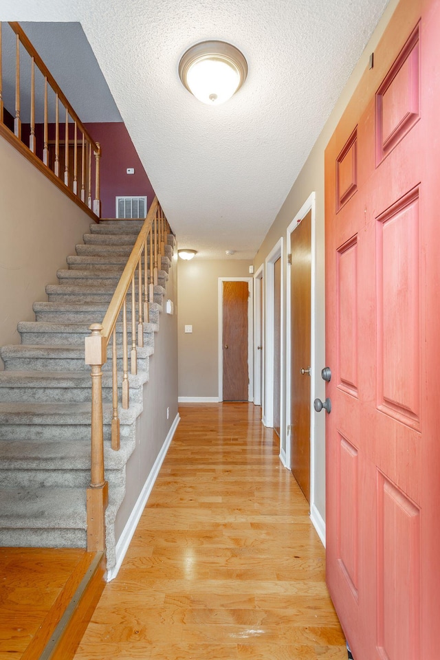 foyer entrance with a textured ceiling, light wood finished floors, visible vents, and baseboards