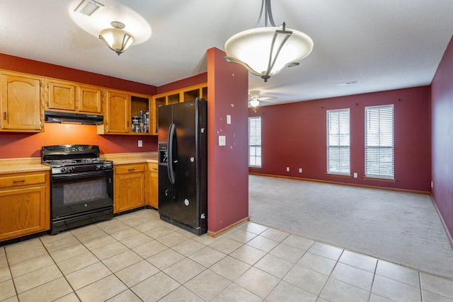 kitchen with under cabinet range hood, light carpet, hanging light fixtures, light countertops, and black appliances