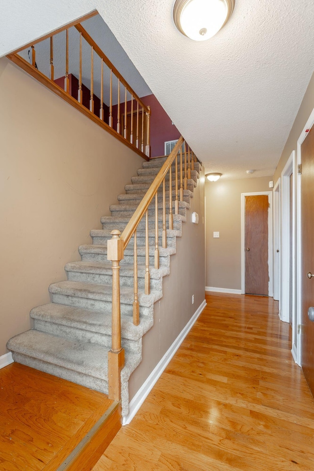 stairs featuring a textured ceiling, wood finished floors, visible vents, and baseboards