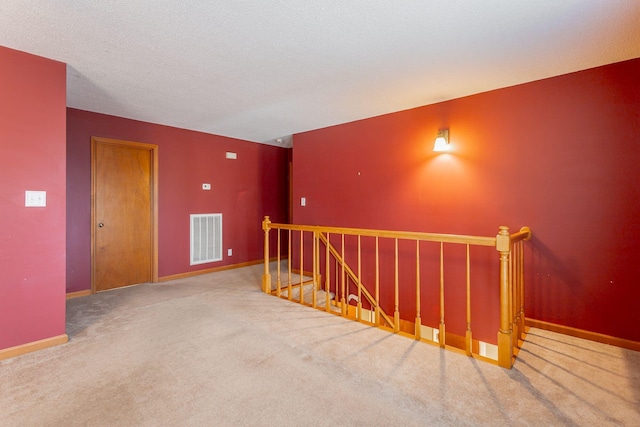 empty room featuring carpet floors, visible vents, a textured ceiling, and baseboards