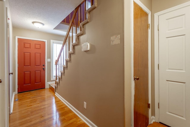 foyer featuring a textured ceiling, light wood-style floors, stairs, and baseboards