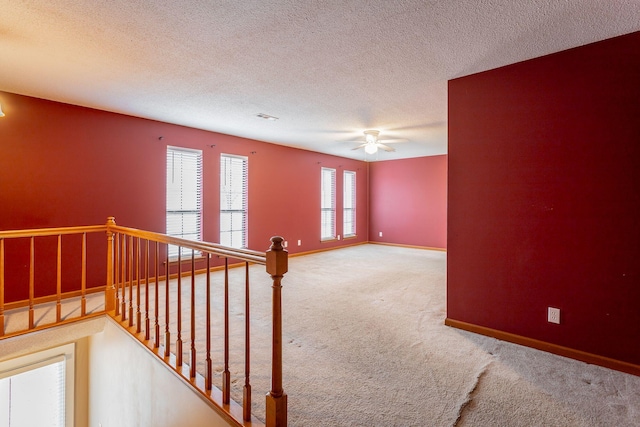 carpeted empty room with visible vents, baseboards, ceiling fan, and a textured ceiling