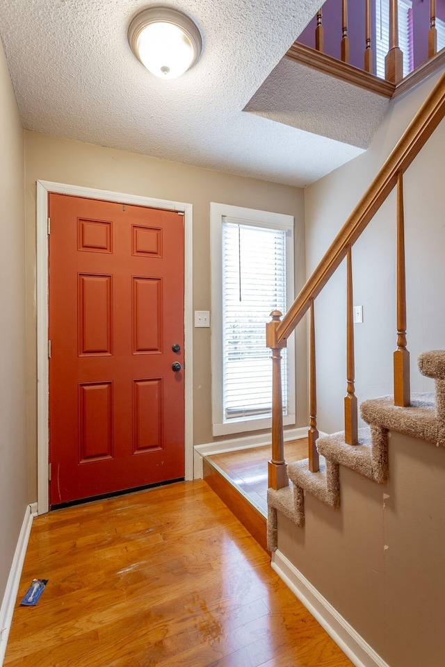 entrance foyer featuring a textured ceiling, stairs, light wood-style flooring, and baseboards