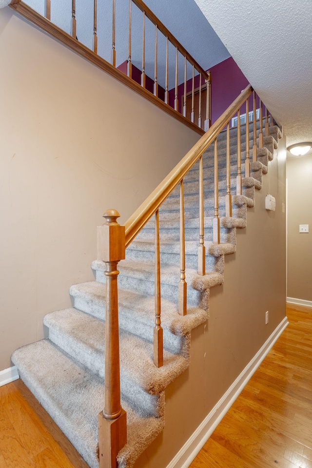 stairway featuring a textured ceiling, baseboards, and wood finished floors