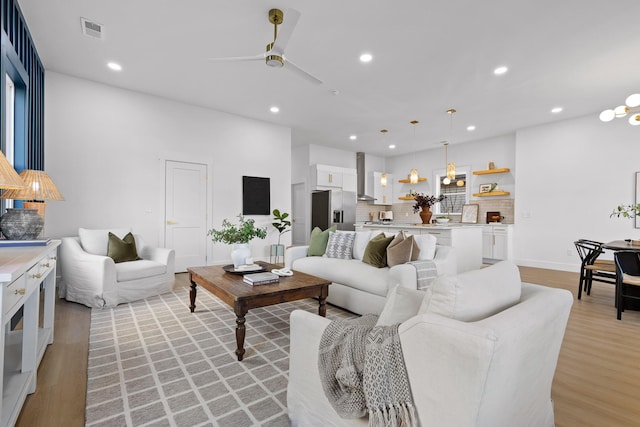 living room featuring ceiling fan with notable chandelier and light hardwood / wood-style flooring