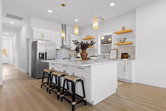 kitchen featuring wall chimney range hood, white cabinetry, a kitchen breakfast bar, a center island, and stainless steel refrigerator with ice dispenser