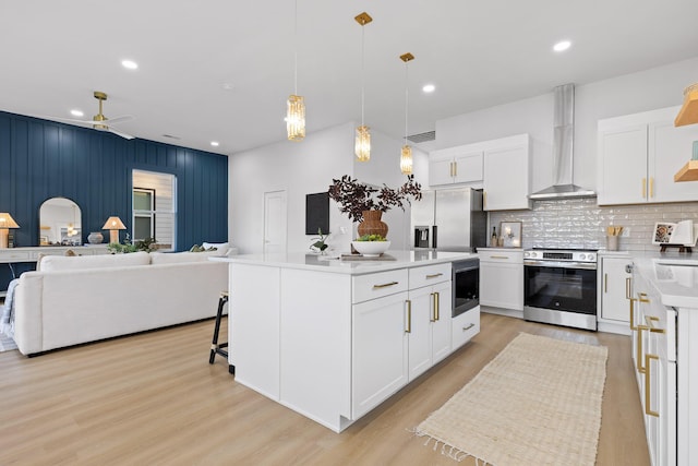 kitchen with wall chimney exhaust hood, a center island, appliances with stainless steel finishes, pendant lighting, and white cabinets