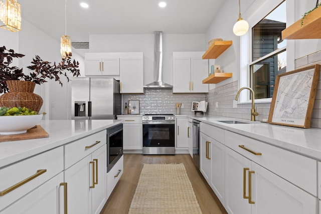 kitchen featuring wall chimney exhaust hood, sink, white cabinetry, light stone counters, and appliances with stainless steel finishes