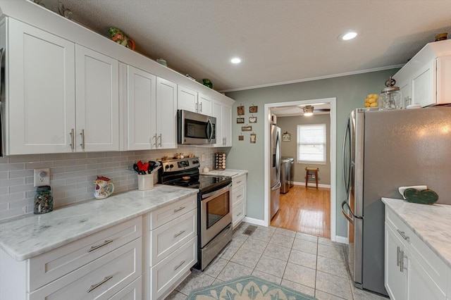 kitchen with stainless steel appliances, white cabinetry, light stone countertops, and backsplash