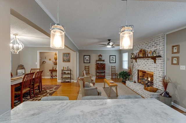 living room featuring ceiling fan, a fireplace, wood-type flooring, ornamental molding, and a textured ceiling