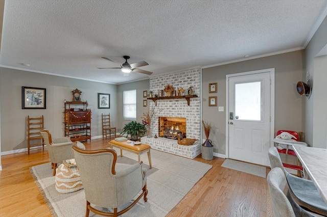 living room with crown molding, ceiling fan, a textured ceiling, a brick fireplace, and light wood-type flooring