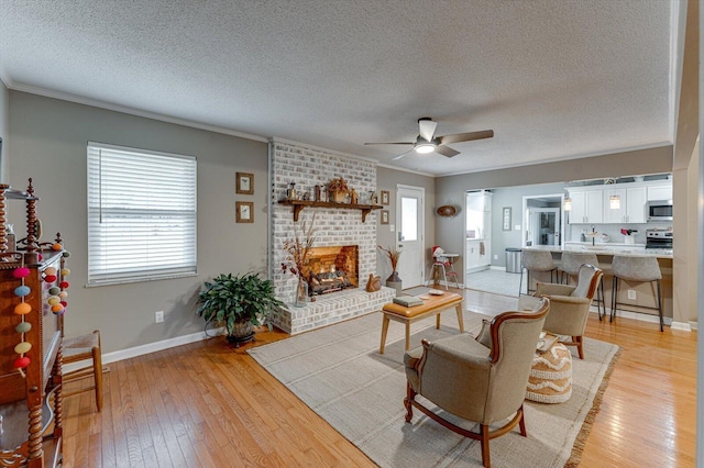 living room featuring a brick fireplace, a textured ceiling, ornamental molding, ceiling fan, and light hardwood / wood-style floors