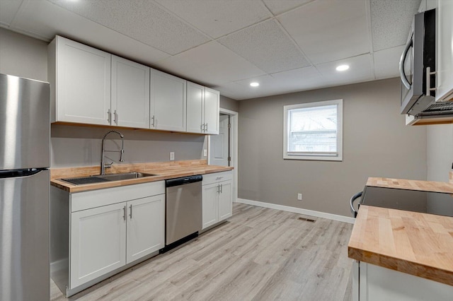 kitchen featuring sink, stainless steel appliances, light hardwood / wood-style floors, white cabinets, and wood counters