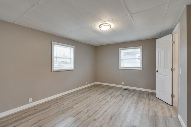 unfurnished room with a wealth of natural light, a paneled ceiling, and light wood-type flooring