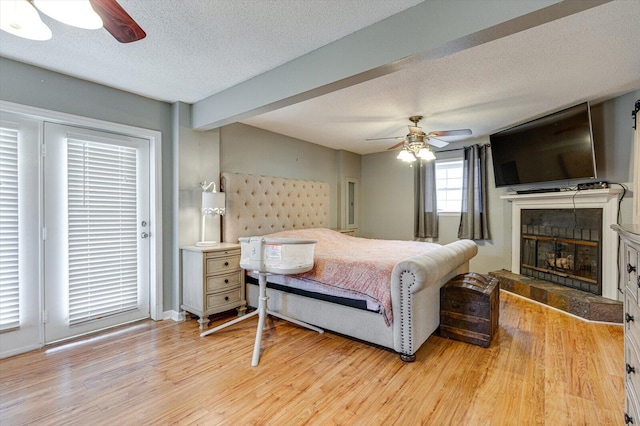 bedroom with a fireplace, beam ceiling, light hardwood / wood-style flooring, and a textured ceiling