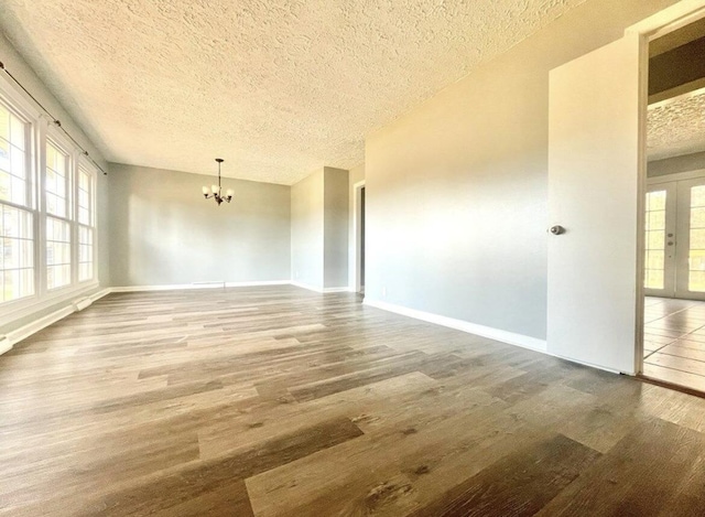 empty room featuring hardwood / wood-style floors, a textured ceiling, french doors, and a chandelier