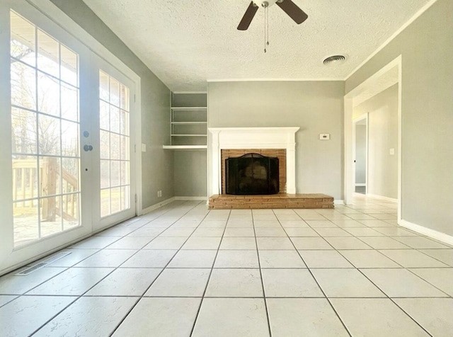 unfurnished living room with light tile patterned floors, a textured ceiling, built in shelves, and a brick fireplace