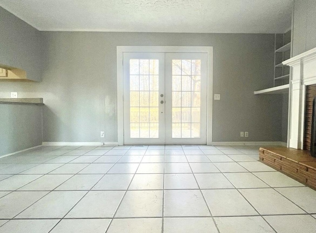 unfurnished living room featuring a brick fireplace, tile patterned floors, french doors, and a textured ceiling