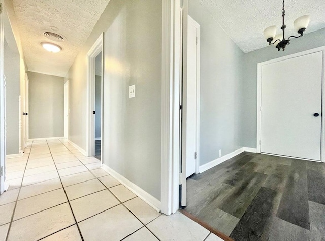 hallway featuring light tile patterned flooring, a chandelier, and a textured ceiling