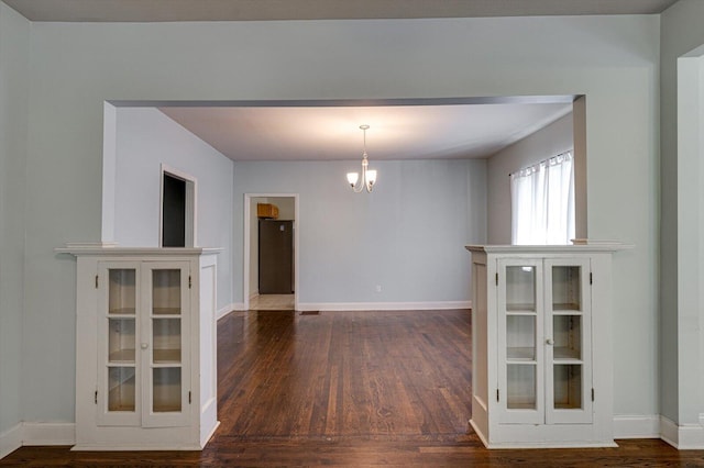 unfurnished dining area with dark wood-type flooring and a notable chandelier