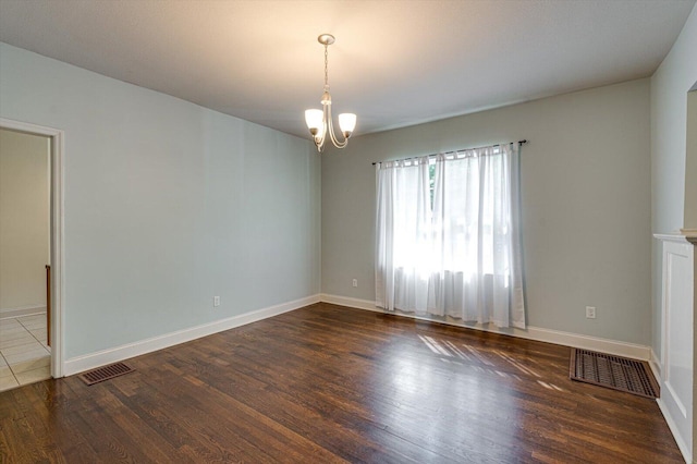 spare room featuring dark hardwood / wood-style flooring and a chandelier