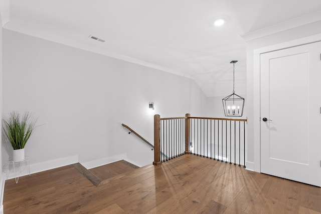 staircase with hardwood / wood-style flooring, a chandelier, and vaulted ceiling