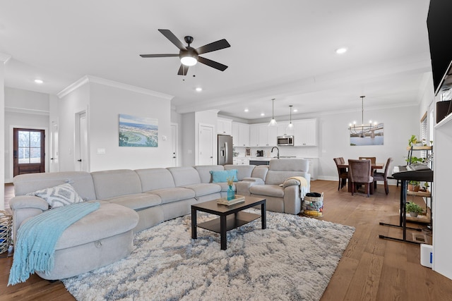 living room featuring sink, hardwood / wood-style flooring, ceiling fan with notable chandelier, and ornamental molding