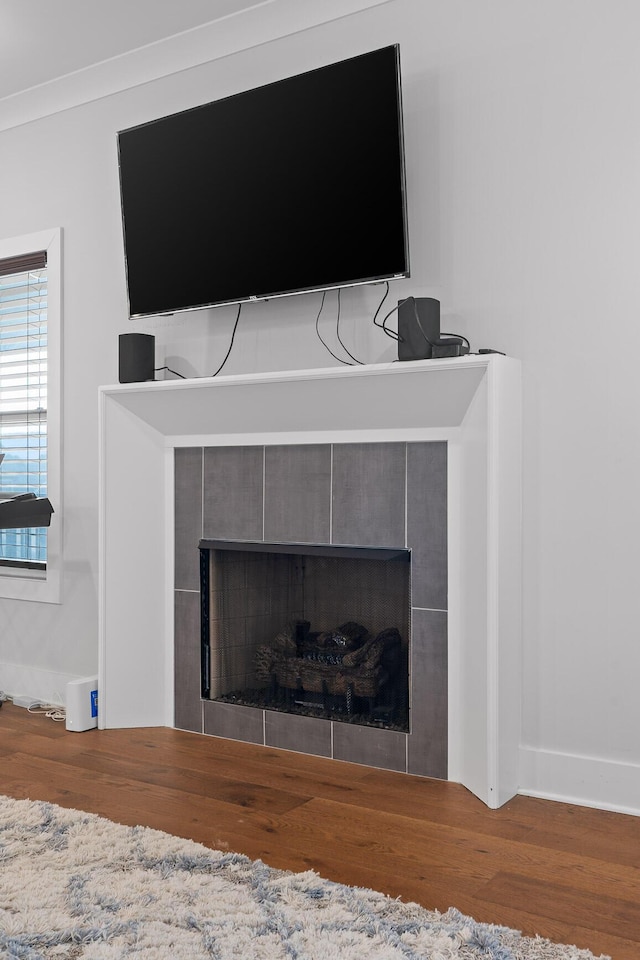 interior details with a tiled fireplace, crown molding, and hardwood / wood-style floors