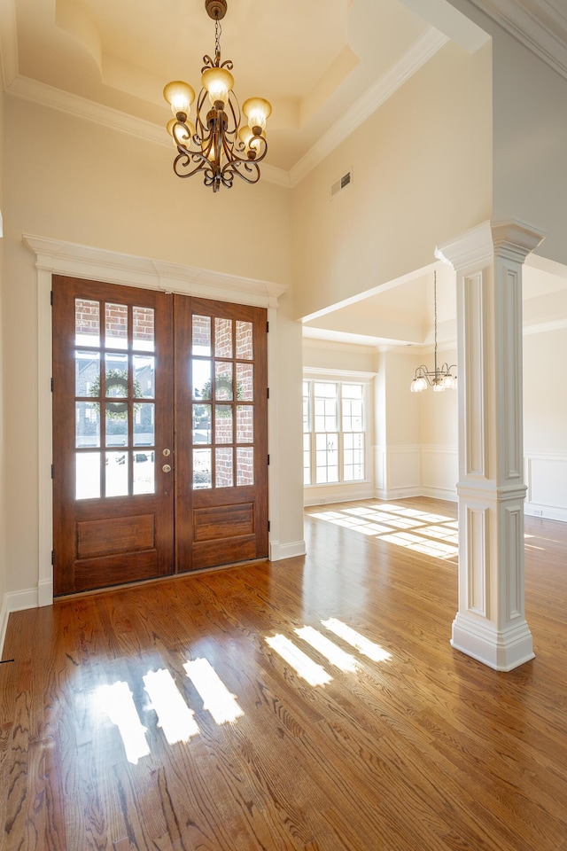 entryway featuring decorative columns, wood-type flooring, a notable chandelier, a tray ceiling, and french doors