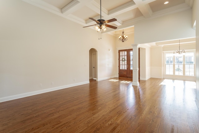 unfurnished living room featuring a towering ceiling, dark hardwood / wood-style floors, ceiling fan with notable chandelier, and ornate columns