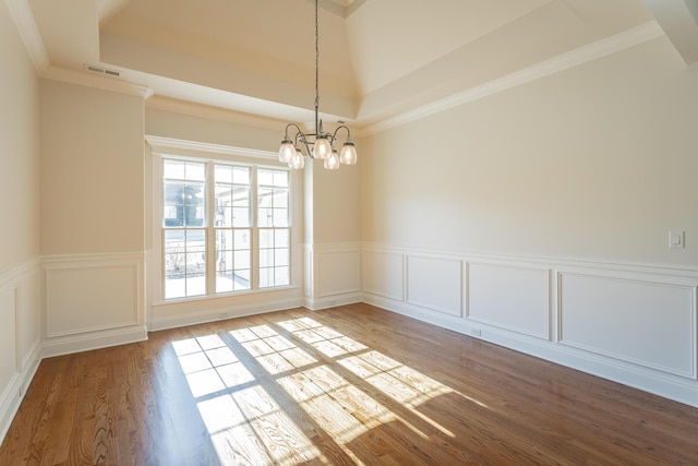 empty room featuring ornamental molding, a chandelier, hardwood / wood-style floors, and a raised ceiling