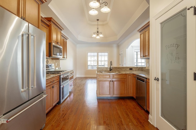 kitchen featuring decorative light fixtures, a raised ceiling, sink, a notable chandelier, and stainless steel appliances