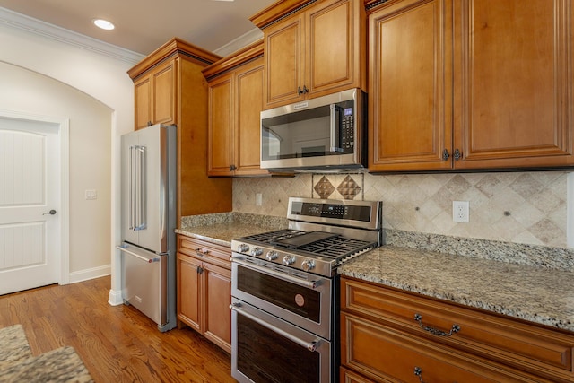 kitchen featuring appliances with stainless steel finishes, backsplash, ornamental molding, light stone counters, and light hardwood / wood-style flooring