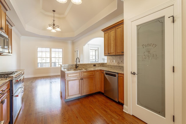 kitchen featuring sink, decorative light fixtures, appliances with stainless steel finishes, a raised ceiling, and hardwood / wood-style floors