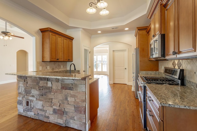 kitchen with kitchen peninsula, hardwood / wood-style flooring, light stone counters, a tray ceiling, and stainless steel appliances