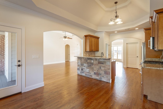 kitchen with ceiling fan with notable chandelier, pendant lighting, ornamental molding, a tray ceiling, and light hardwood / wood-style flooring