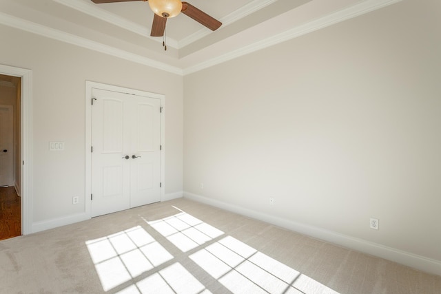 unfurnished bedroom with crown molding, light carpet, a raised ceiling, a closet, and ceiling fan