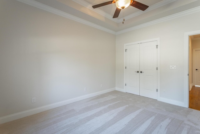 unfurnished bedroom with light colored carpet, ceiling fan, a raised ceiling, crown molding, and a closet