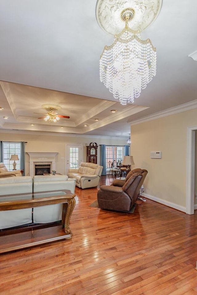 living room with crown molding, ceiling fan with notable chandelier, a raised ceiling, and light hardwood / wood-style floors