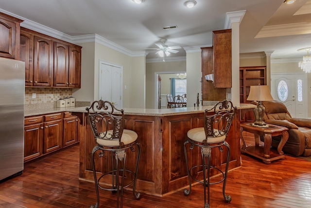 kitchen with stainless steel refrigerator, a kitchen breakfast bar, light stone counters, ornamental molding, and kitchen peninsula