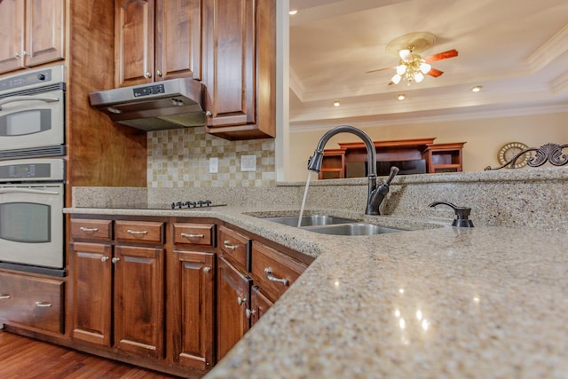 kitchen featuring double oven, sink, light stone counters, a tray ceiling, and crown molding