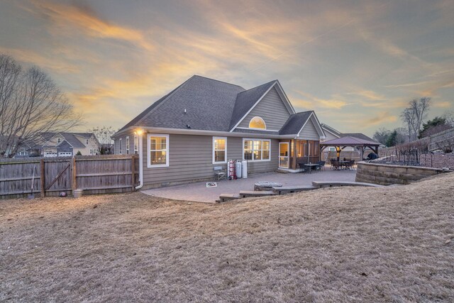 back house at dusk with a gazebo, a fire pit, and a patio area