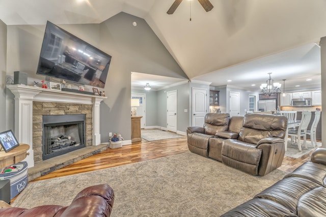 living room featuring a stone fireplace, ceiling fan with notable chandelier, high vaulted ceiling, crown molding, and light hardwood / wood-style flooring