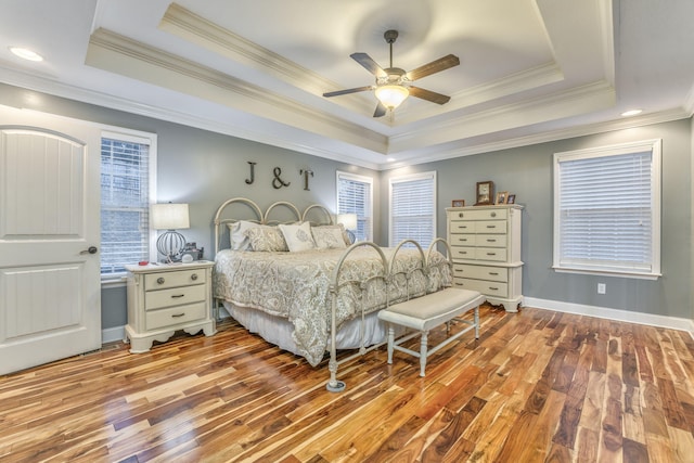 bedroom featuring a raised ceiling, crown molding, ceiling fan, and light wood-type flooring