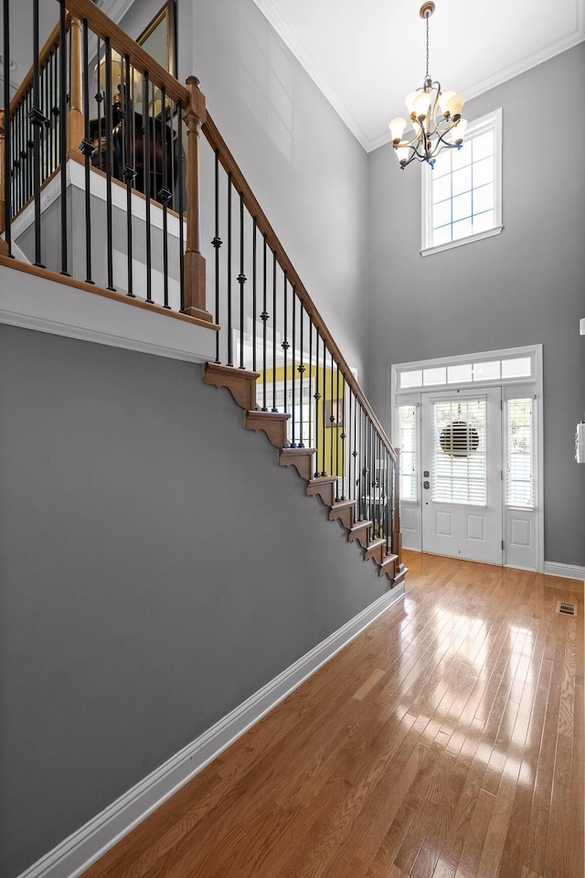 foyer with ornamental molding, a towering ceiling, hardwood / wood-style floors, and a chandelier