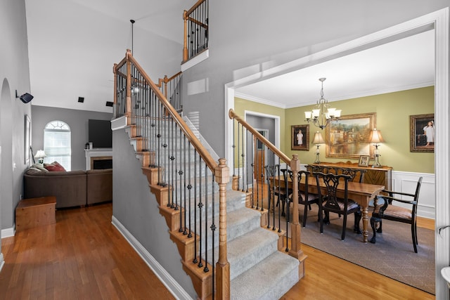 stairs with a high ceiling, wood-type flooring, ornamental molding, and a notable chandelier