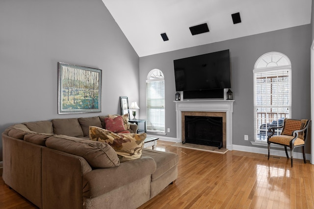 living room with a tiled fireplace, high vaulted ceiling, light hardwood / wood-style floors, and a healthy amount of sunlight