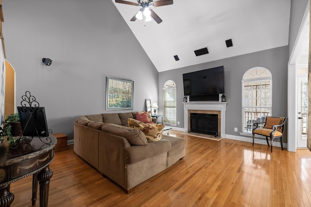 living room featuring high vaulted ceiling, a tile fireplace, ceiling fan, and light wood-type flooring