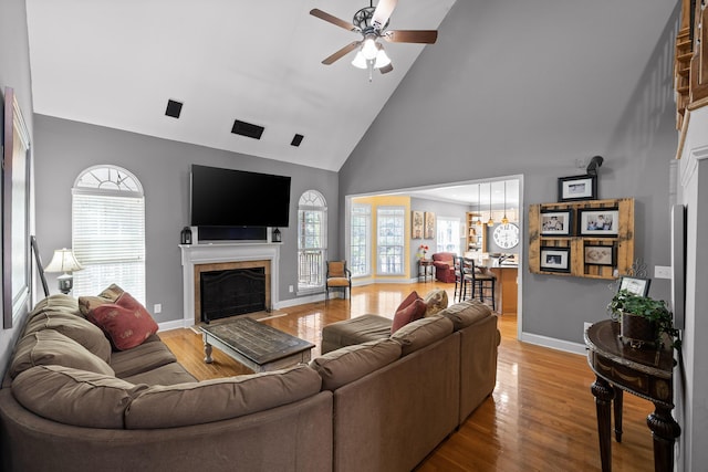 living room featuring a tiled fireplace, high vaulted ceiling, hardwood / wood-style flooring, and ceiling fan